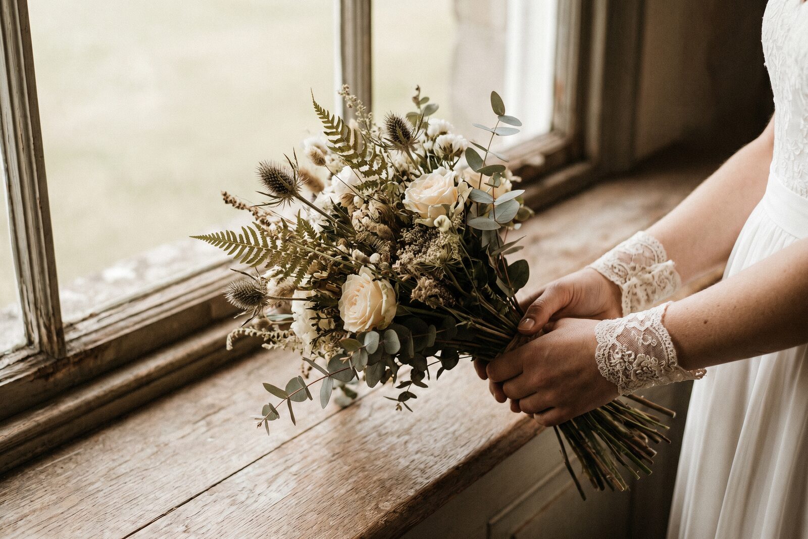 A bride holding a wildflower bouquet by a window